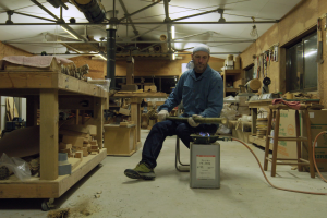 Man sits in a craft workshop with a bamboo flame over a controlled flame.