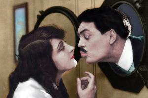 Max Linder is kissing a woman in a movie scene.