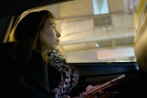 Chinese-American woman holds her phone in her hand while staring out the window of a taxi cab.