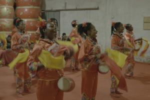 A group of Nigerian women perform a Chinese dance in traditional orange-colored Chinese dress.
