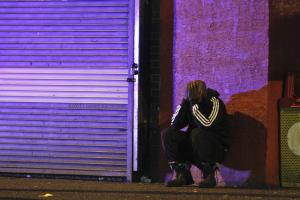 A Black Man in a track suit leans against a city strip wall with his head in his hands