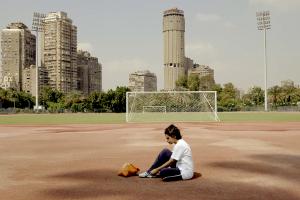 A teenager sitting in the middle of a soccer field.
