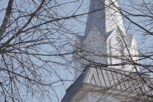 Photo of a white steeple partially hidden behind bare tree branches. 
