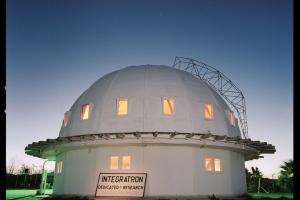 A white dome research center sits on a green lawn at dusk with stars shining in the sky above