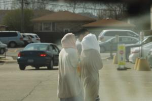 two women dressed in traditional muslim attire walk through parking lot with male 