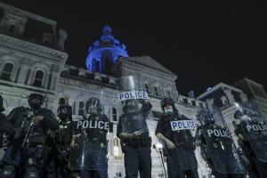 A line of Baltimore police officers wearing riot gear and holding shields stand in front of city hall the night after the murder of George Floyd.