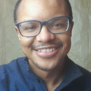 Headshot of Terence Johnson, a Black man with short hair, wearing a blue shirt and blue glasses.