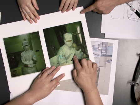 Photographs are laid out on a table of individuals in hazmat suits. Several pairs of hands are pictured in frame handling these pictures.
