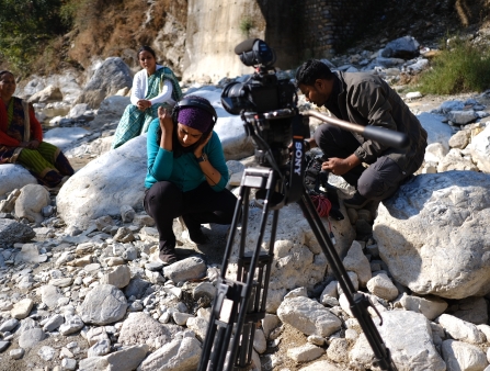A woman kneels while listening through a pair of headphones.