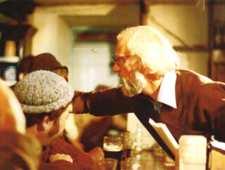 In a crowded bar, a man reaches over the bar.