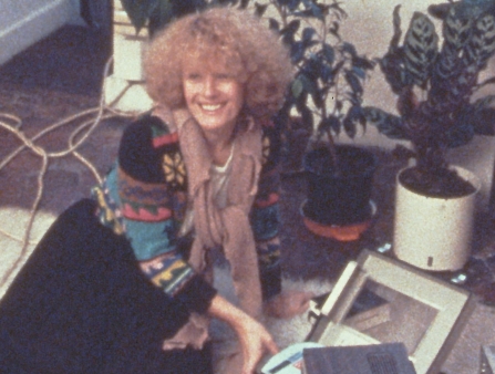 A woman with curly hair splays on the floor on a rug, smiling.