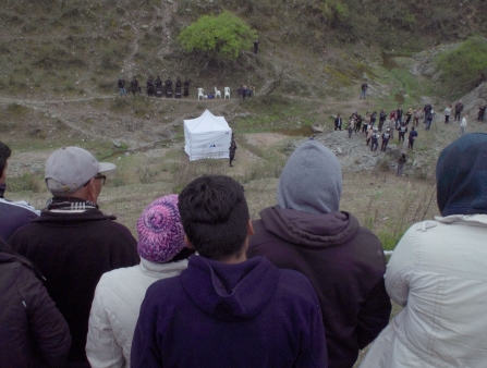 A group of people stare at a white tent erected on a hillside.