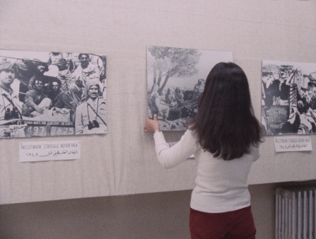 A young woman with shoulder-length hair hangs a photograph on a gallery wall.