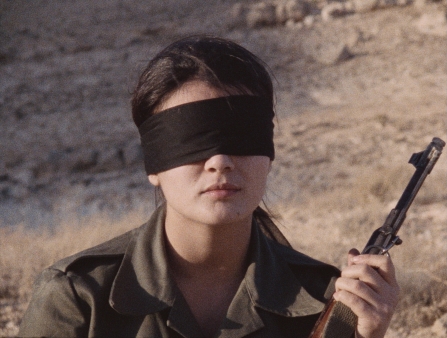 A woman wearing a black blindfold holds a rifle.
