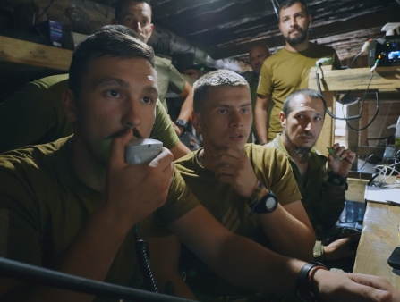 Six anxious looking soldiers in a cramped space full of wires and communication devices