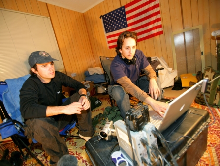 Two brothers sit in a wood-paneled room with an American flag.