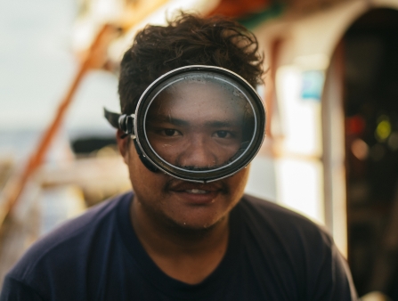 A man wearing swim goggles on the deck of a fishing boat.