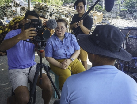 A film crew films an interview on the shore.