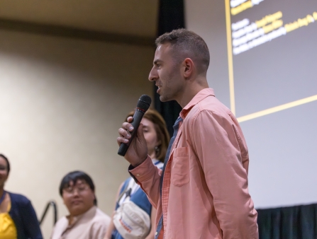 Man with short-cropped hair holds a mic next to three female panelists