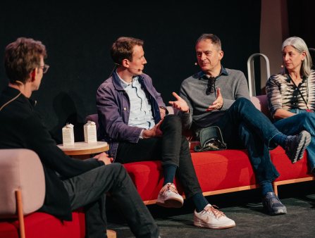 Four people sit on red couches on a panel.