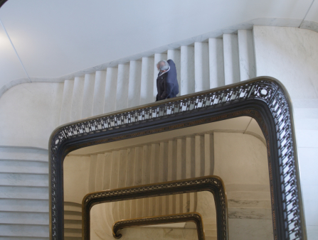 Shot from above of an older man in a suit going down an imposing marble staircase