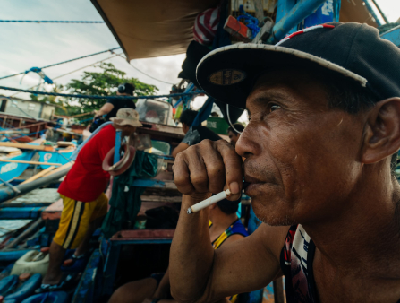 A man smokes a cigarette at a crowded dock.