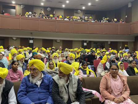 An auditorium and balcony with a full house, many wearing yellow turbans.