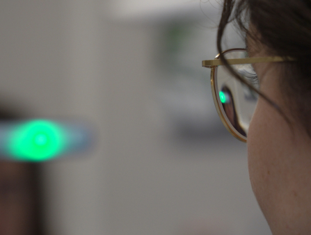 A young woman with dark hair and glasses in close up from behind at a medical facility
