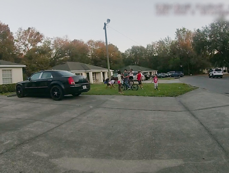 160 point of view shot of a neighborhood driveway with a group of kids playing on a patch of grass.
