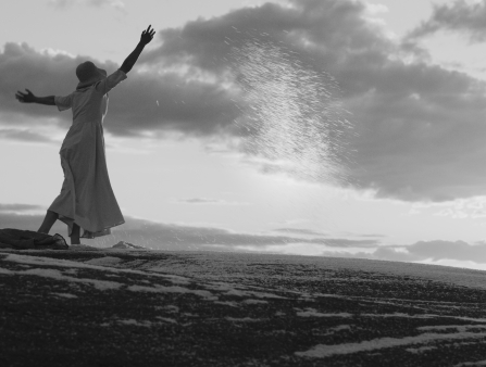 Black and white shot of a woman in a cloche hat and dress scattering something along her path
