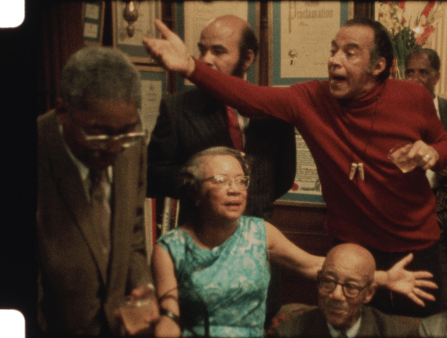 Grainy photo of a group of older Black men and women arguing in a living room