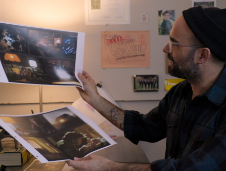 A white man with a beard, glasses and a beanie sits at his desk showing two mood boards for Stranger Things production design