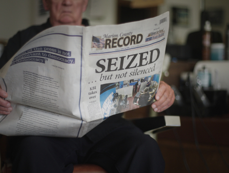 A man holds a newspaper with the headline: "SEIZED."