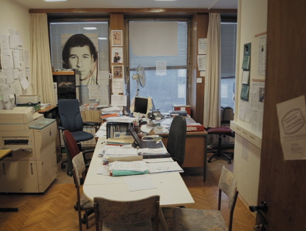 An empty, cramped office with plenty of strewn papers and posters covering every wall