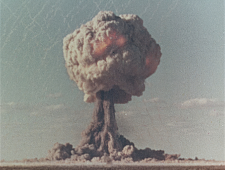 Shot of an atomic mushroom cloud arising above a barren field