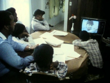 A black working family sits at the table watching the television