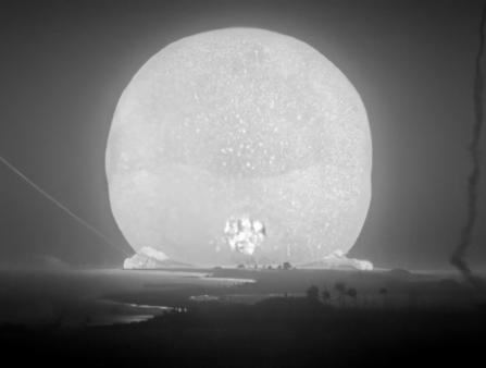 Black and white shot of a large beam of light mushrooming following an atomic bomb
