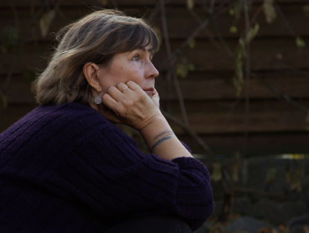 Close-up of a middle-aged white woman with short brown hair in a dark purple sweater holding her face against her hands