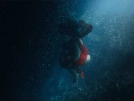 Dark shot of a woman in a red dress floating underwater, her black hair curling up