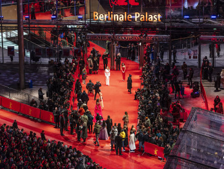 Outdoor, nighttime shot of a red carpet at the Berlinale Palast where photographers crowd folks dressed up near them