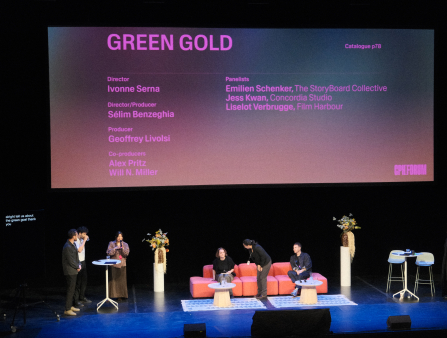 A brightly-lit photo of a number of folks seated at a theater stage for a panel titled "Green Gold," as shown by the screen behind them all.