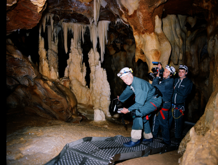 Three middle-aged white men in gear and holding cameras pose for a photo inside a cave lit only by the flash of the camera