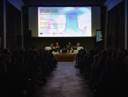 A packed theater with a screen announcing a CPH:DOX panel features four people seated at a stage holding mics mid-conversation