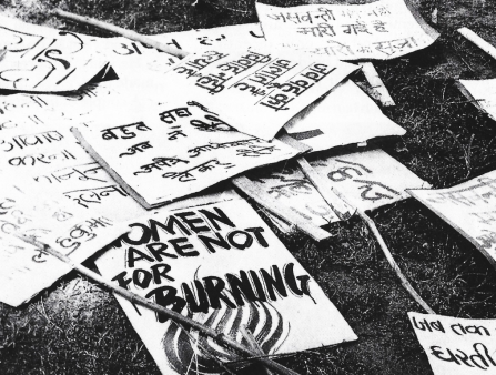 Black and white shot of protest posters on the ground including one that reads "Women Are Not For Burning"