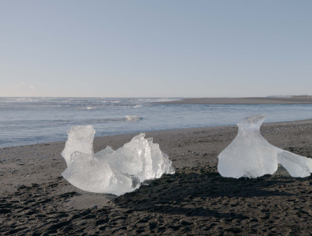 Two pieces of ice are seen melting on a sandy beach