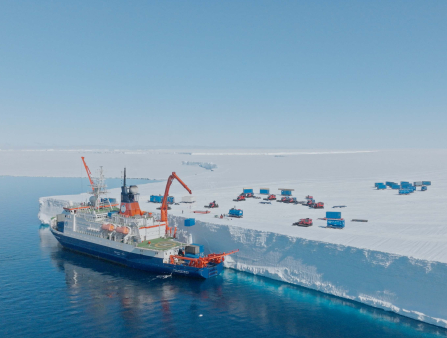 Wide shot of a ship carrying containers parked next to a frozen snow-capped landscape