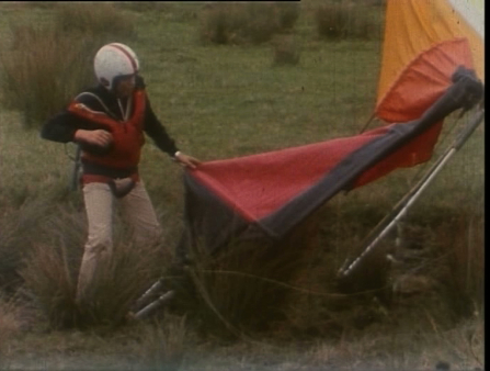 A man with a helmet on and khaki pants looks onto the parachute that's unfurled next to him