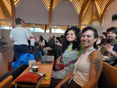 Seated at a narrow wooden table, two women smile.