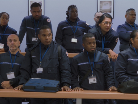 14 uniformed guards stand in two rows behind long tables