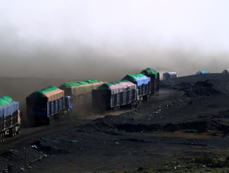 A line of covered trucks drive over black terrain